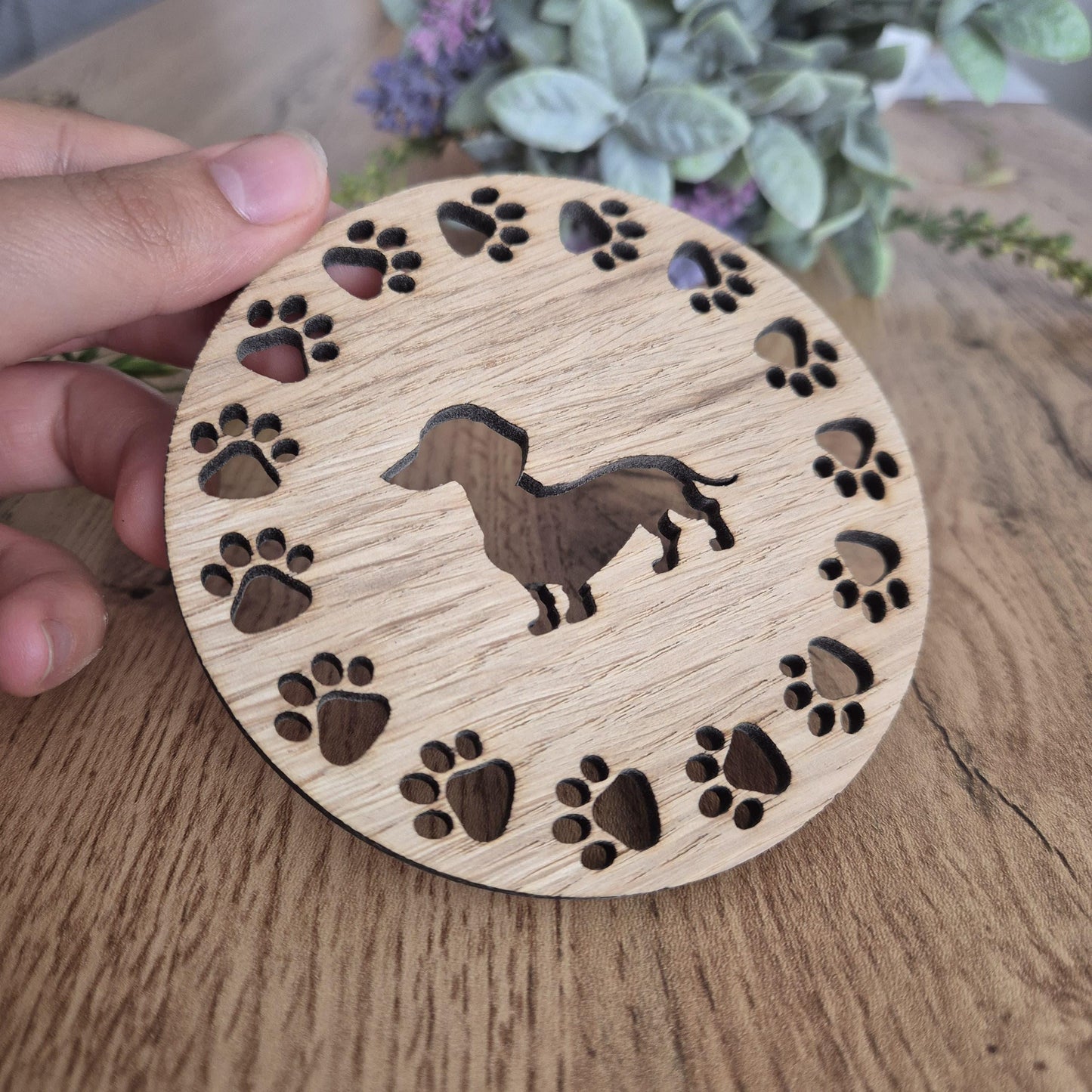 A wooden round coaster with a sausage dog in the middle, with paw prints all around the outside.