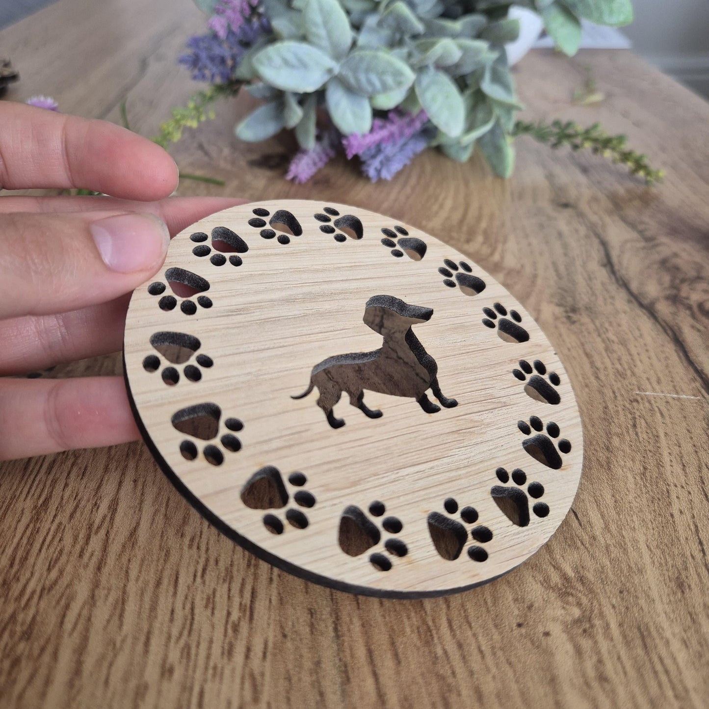 A wooden round coaster with a sausage dog in the middle, with paw prints all around the outside.