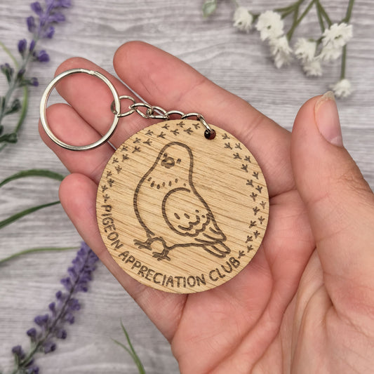 A person's hand holding a wooden keychain with a bird engraved on it.