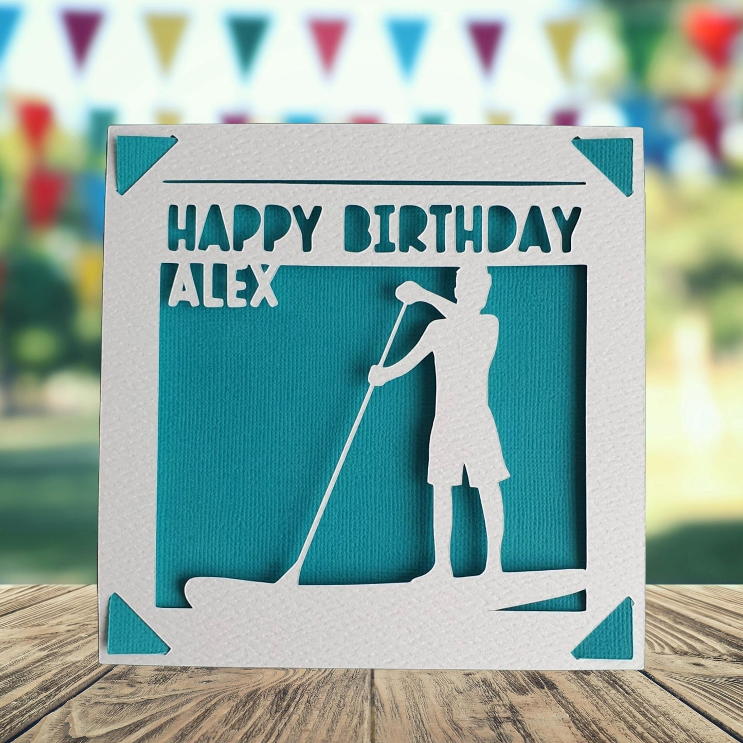 A personalised birthday card with a paddleboarding theme, featuring a silhouette of a person paddleboarding on a body of water. The card is white with turquoise accents and text, and includes a personalised message with the name of the recipient