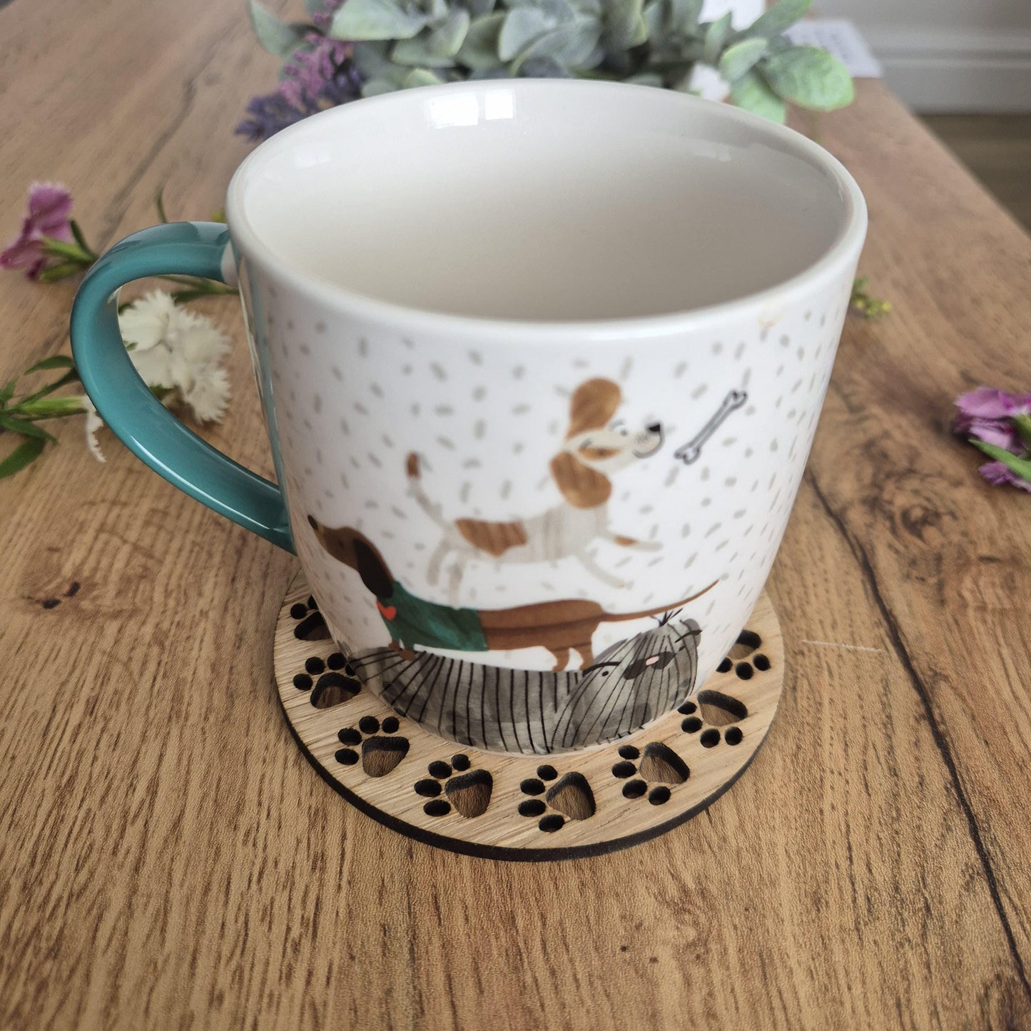 A wooden round coaster with a sausage dog in the middle, with paw prints all around the outside.