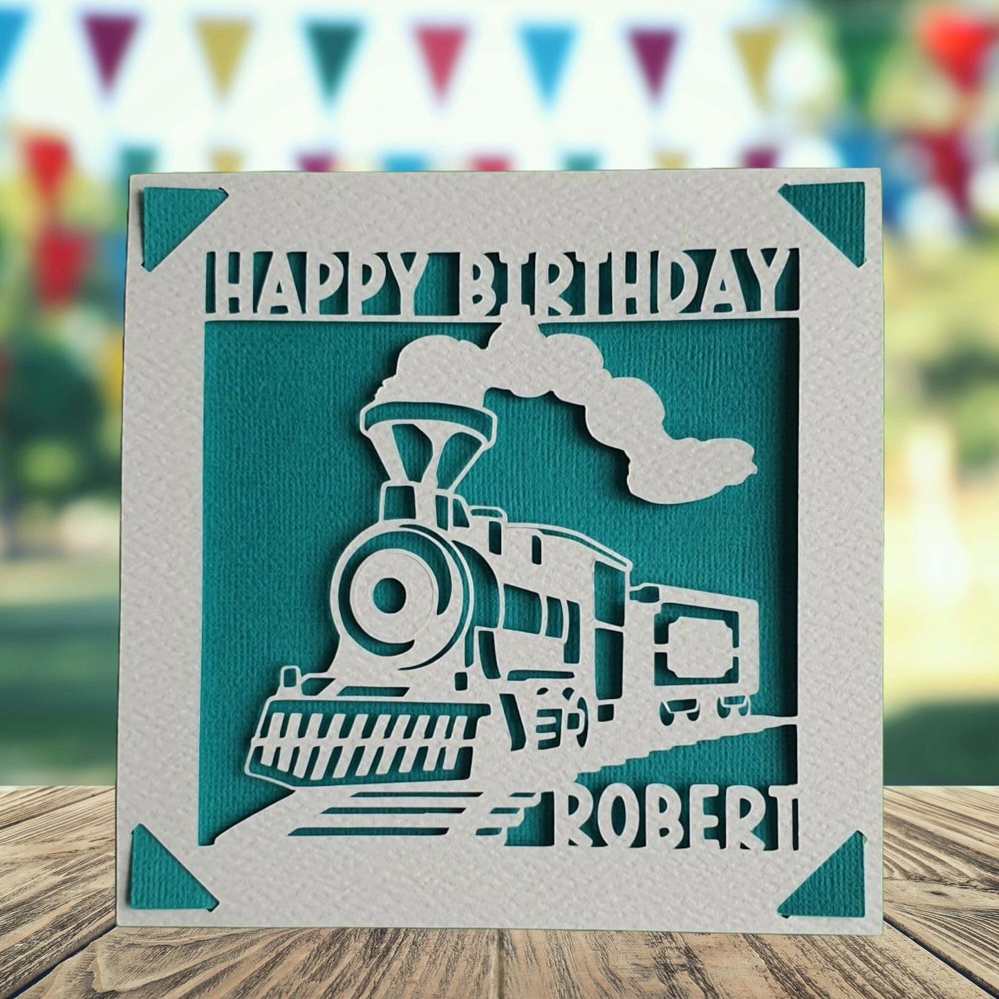 A personalised birthday card with a train illustration, made from hammered white card, with the name of the recipient printed on it. The card has a turquoise background.