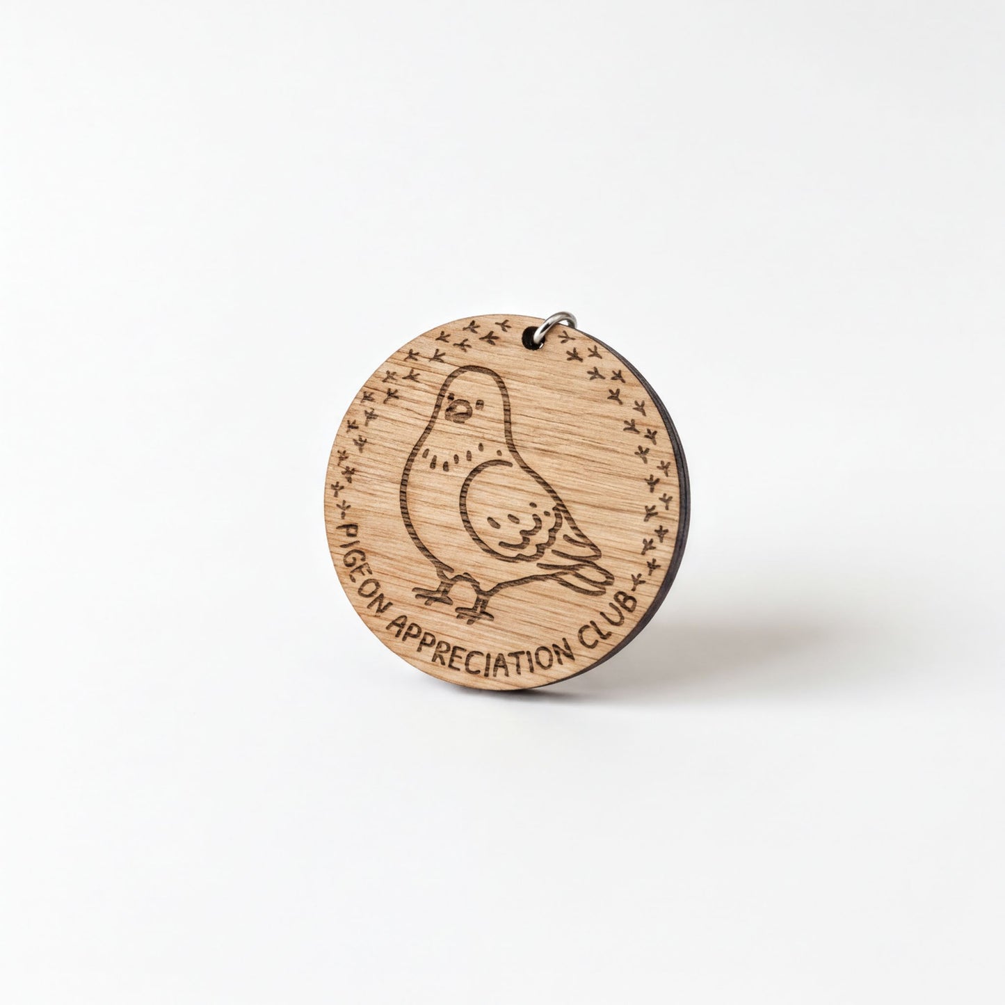 A wooden keychain with a bird engraved on it, and the text "Pigeon Appreciation Club" around the edge.