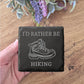 A hand holding a slate with a graphic of a hiking boot and the text "I'D RATHER BE HIKING" printed on it.