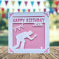 A white greeting card with a silhouette of a person kneeling, playing crown green bowling and a banner with a star, placed on a wooden surface.