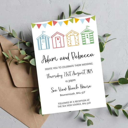A beach hut themed wedding invitation with colourful huts, personalized with the names of the couple and the details of the wedding venue, placed on a kraft brown envelope. Made from textured quality cardstock.