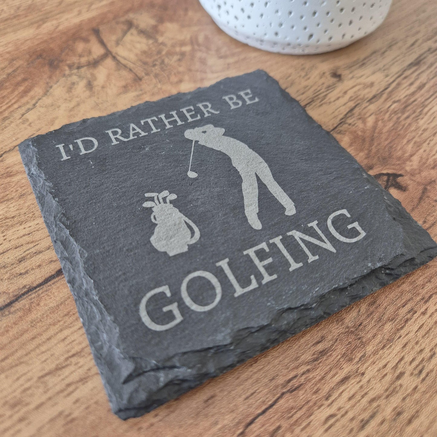 A square natural slate coaster with the phrase 'I'd rather be GOLFING' engraved on it and a silhouette of a person playing golf in the centre.