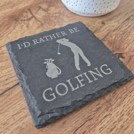 A square natural slate coaster with the phrase 'I'd rather be GOLFING' engraved on it and a silhouette of a person playing golf in the centre.