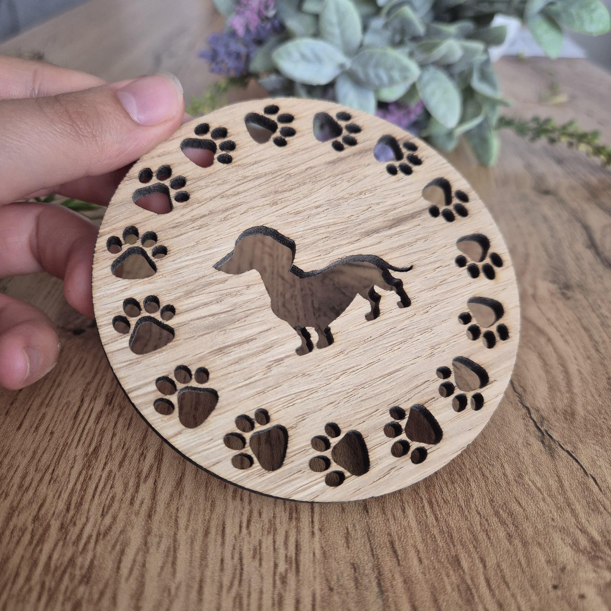A wooden round coaster with a sausage dog in the middle, with paw prints all around the outside.
