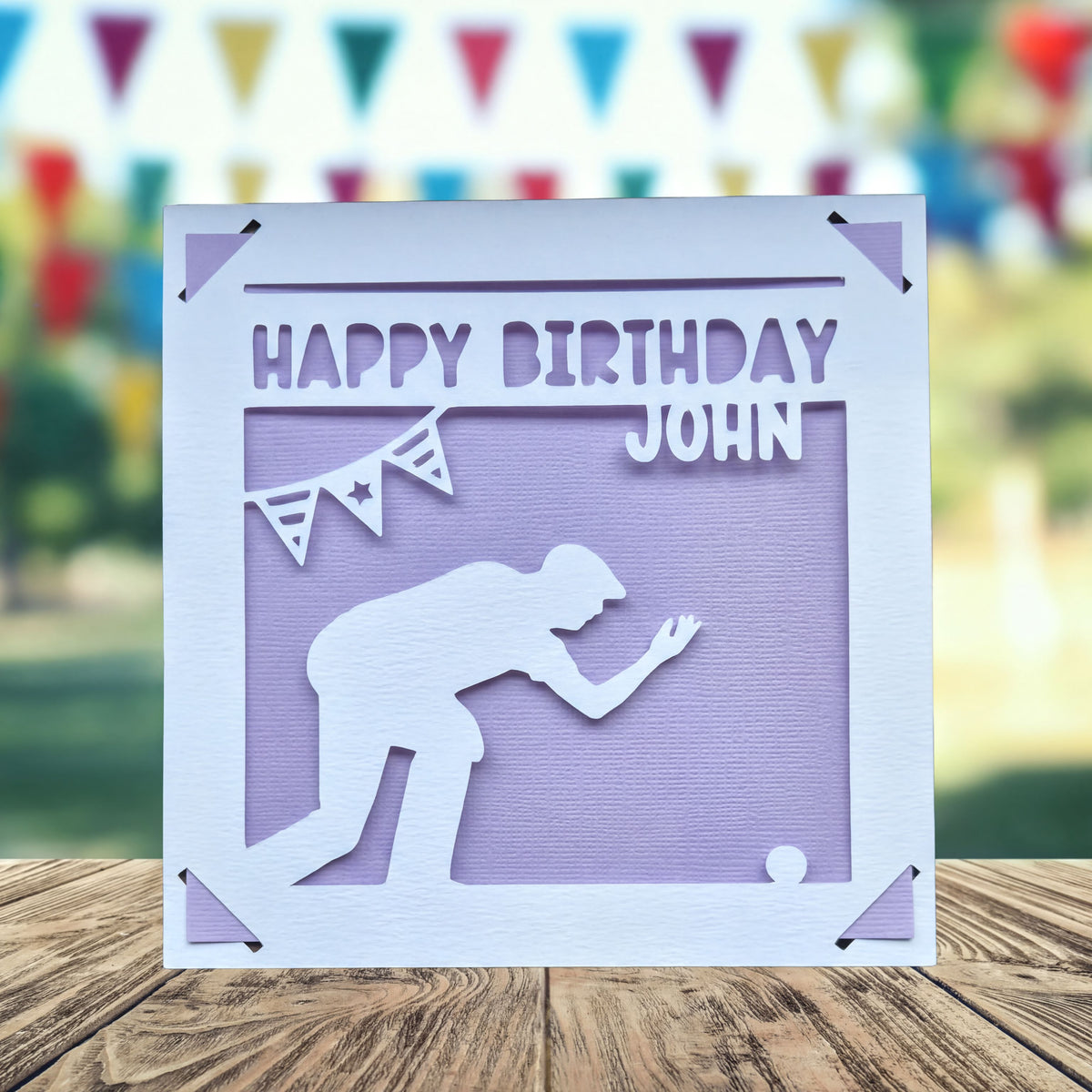 A white greeting card with a silhouette of a person kneeling, playing crown green bowling and the text "Happy Birthday John" printed on it.