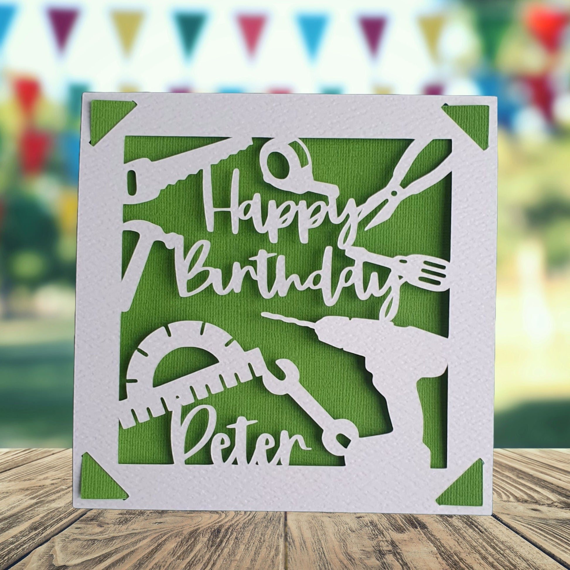 A personalized happy birthday card with a green background, featuring a silhouette of a screwdriver, drill, spanner, hammer, plyer, and other tools, with the text 'Happy Birthday' and a space to add a name and age if required.