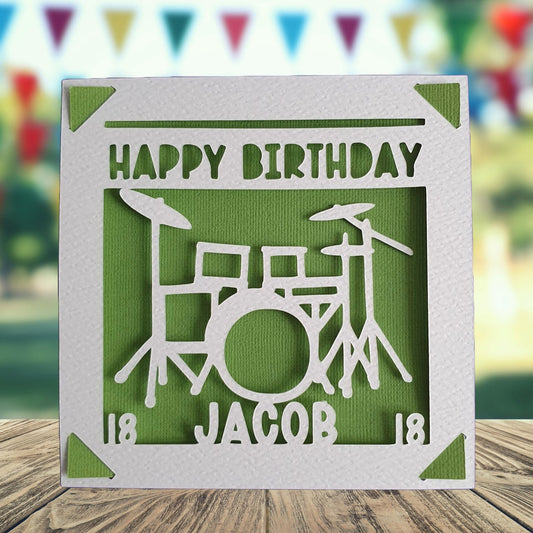 A personalised birthday card with a green drum design on the front, with the text 'Happy Birthday' and a space to add a name and age if required. Green background.