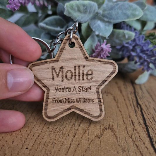 A personalised engraved wooden star shaped keyring from teachers to give as gifts to their pupils for the end of the school year. The keyring is engraved with the student's name, the text 'you're a star!' and the teacher's name.
