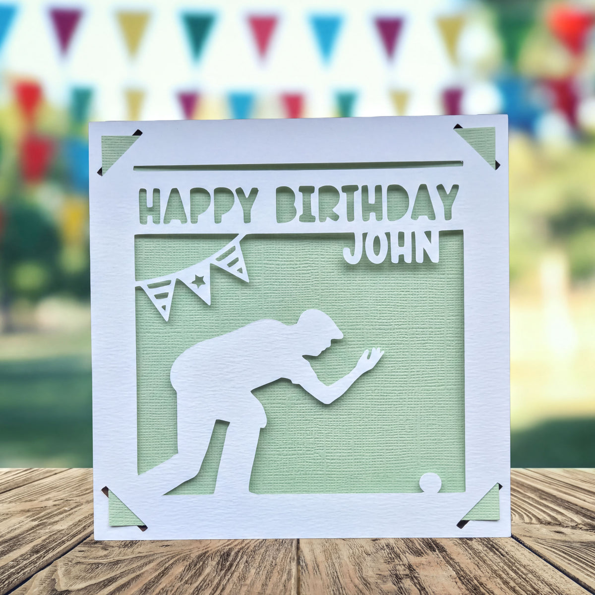 A white greeting card with a silhouette of a person kneeling, playing crown green bowling and the text "Happy Birthday John" printed on it.