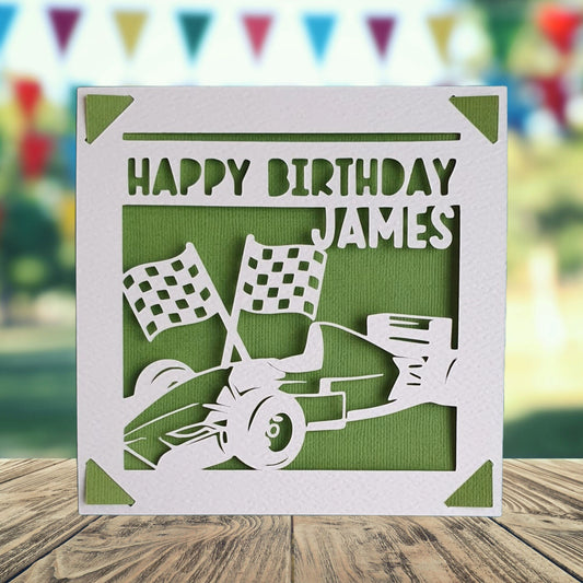 A personalised birthday card with a green background, featuring a racing formula one car and checkered flag graphics, with the name of the recipient printed on the front.