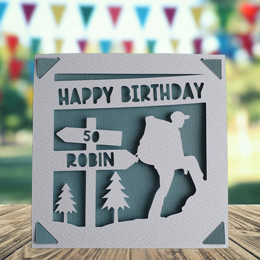 A personalised birthday card with a hiking theme, featuring a silhouette of a hiker and trees in the background. The card is white with text and has a teal background.