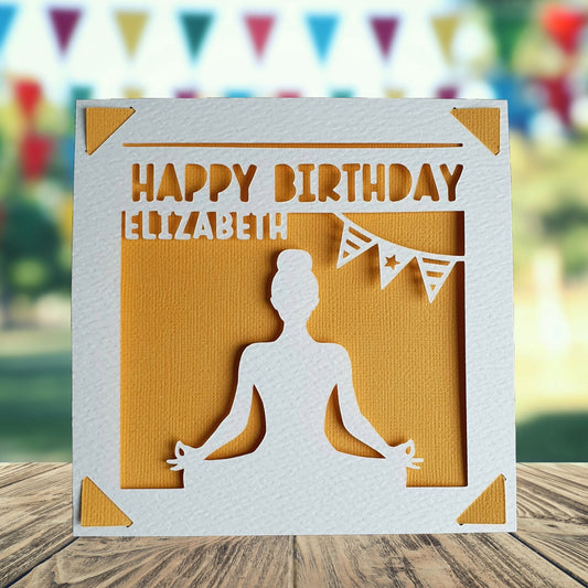 A personalised birthday card with a white background featuring a cut-out design of a person meditating. The card reads 'Happy Birthday' and has the name of the recipient printed on it. The background is orange.