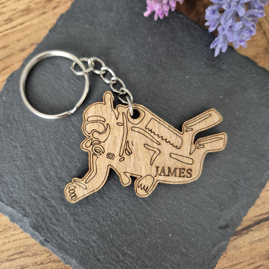 A personalised wooden keyring of a scuba diver, personalised with a name. The name is engraved on the wood. The keyring is silver.