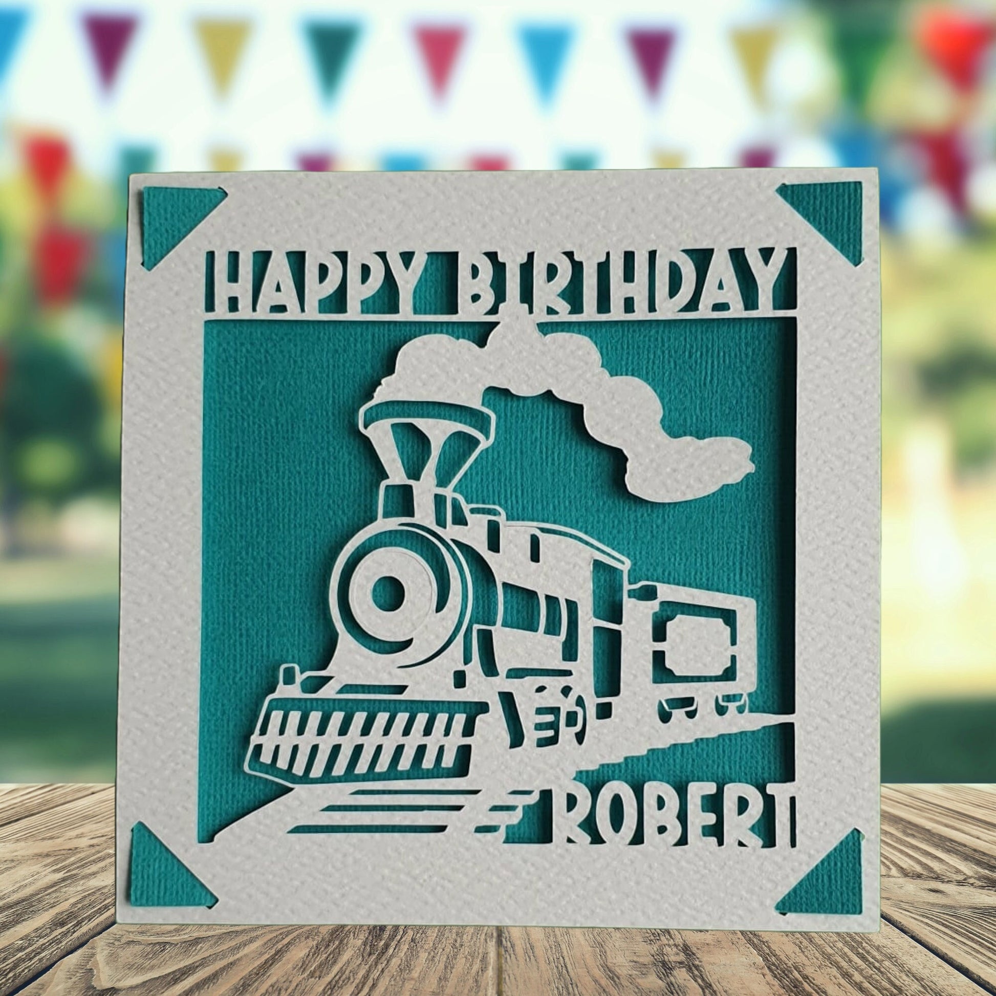 A personalised birthday card with a train illustration, made from hammered white card, with the name of the recipient printed on it. The card has a turquoise background.